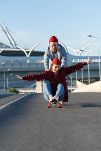 Young hipster couple have fun on longboard outdoors riding city road cheerful laughing together