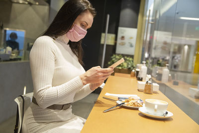 Young woman using mobile phone while sitting in cafe