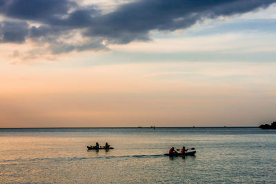 People in sea against sky during sunset