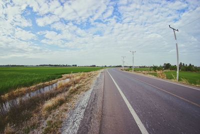 Road by agricultural field against sky