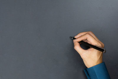 High angle view of human hand holding pen against gray background