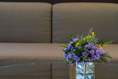 Close-up of purple flower vase on desk and sofa at home