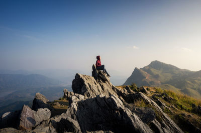 Side view of woman sitting on mountain against blue sky