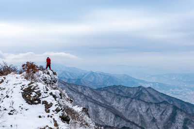 Rear view of hiker standing on snowcapped mountain against cloudy sky