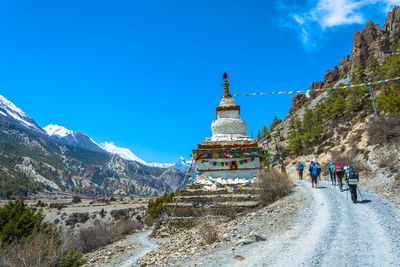 People hiking by temple on snow covered landscape against blue sky