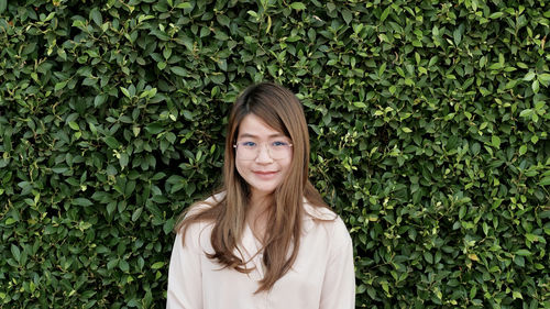 Portrait of young woman standing against plants