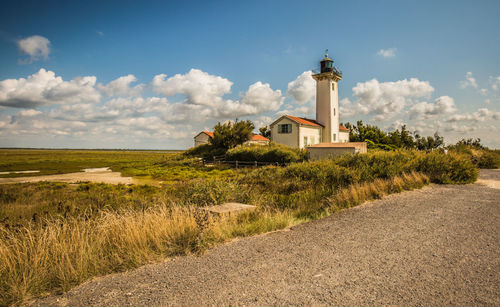 Lighthouse on landscape against cloudy sky