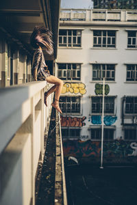 Full length of young woman tossing hair while sitting on retaining wall