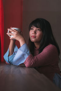 Young woman looking away while drinking coffee at home