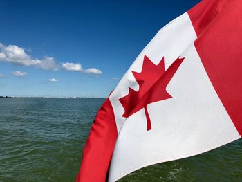 Close-up of canadian flag on sea against blue sky