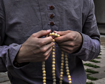 Midsection of man holding religious beads while standing outdoors