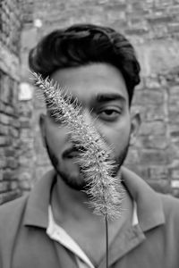 Portrait of young man holding reed against wall