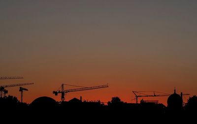 Silhouette cranes at construction site against sky during sunset