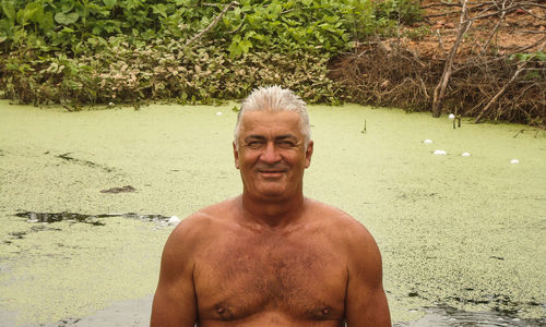 Portrait of shirtless man standing against water