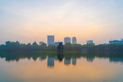 Scenic view of lake by buildings against sky during sunset