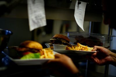 Cropped image of hands holding plates with burgers and french fires