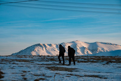 Rear view of men walking on snowcapped mountain against sky