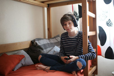 Teenager with a phone and headphones listening to music on the first floor of a bunk bed, 