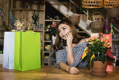 Woman with shopping bags talking on mobile phone at table in shop