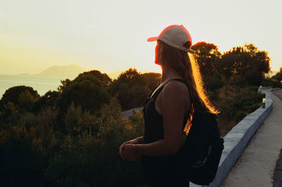 Rear view of woman standing on field against sky during sunset