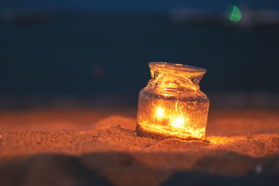 Close-up of illuminated glass jar on sand at night