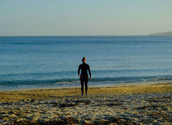 Rear view of woman standing at beach against clear sky