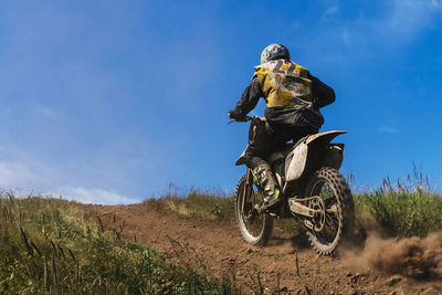 Rear view of man riding motorcycle on field against sky