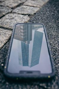 High angle view of phone with modern building reflection on footpath