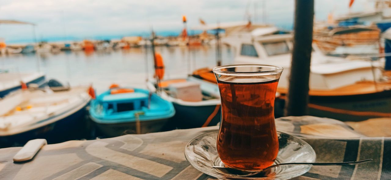 water, nautical vessel, food and drink, drink, focus on foreground, sea, refreshment, moored, alcohol, transportation, vehicle, no people, nature, boat, table, harbor, wood, travel destinations, sky, ship, drinking glass, travel, glass, mode of transportation, day, household equipment, outdoors, beach, pier, land, vacation, tourism