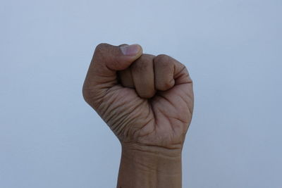 Cropped hand clenching fist against blue sky