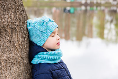 A lonely sad girl stands with closed eyes by a tree on the shore of the lake. mental health.