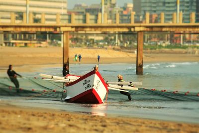 Fishermen working by fishing boat moored on sea shore