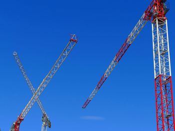 Low angle view of cranes against clear blue sky