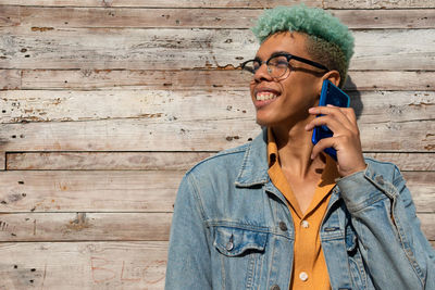 Smiling young man using mobile phone standing on wood