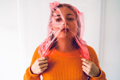 Portrait of teenage girl with plastic bag covering face standing against wall