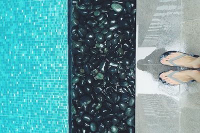 Low section of woman standing by pebbles at poolside