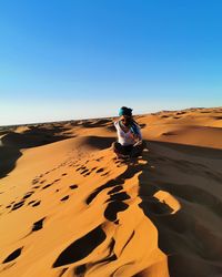 Rear view of man riding motorcycle on desert against clear sky