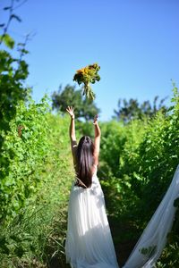 Rear view of bride throwing bouquet while standing on field against sky