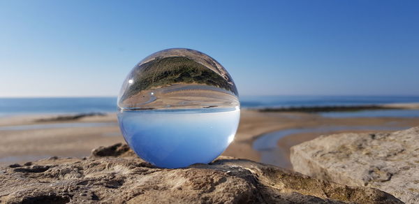 Close-up of water on rock at beach against clear blue sky