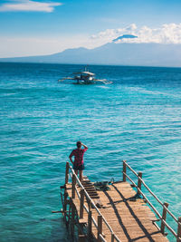 Rear view of man standing on pier at sea against sky