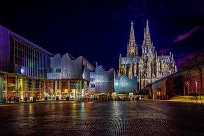 Illuminated buildings and cologne cathedral against sky at night