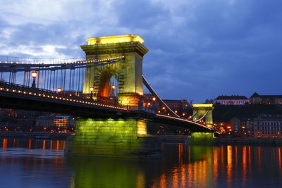 Illuminated bridge over river against sky in city