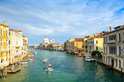 High angle view of boats in canal amidst buildings against cloudy sky