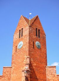 Low angle view of a line-symmetrical brick clock tower against blue sky