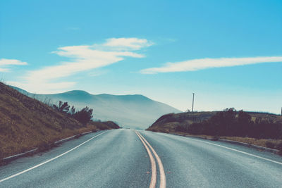 Empty road leading towards mountains against sky