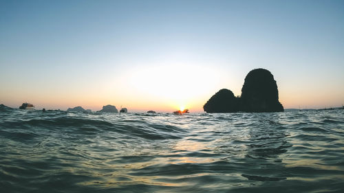 Silhouette rocks in sea against clear sky during sunset