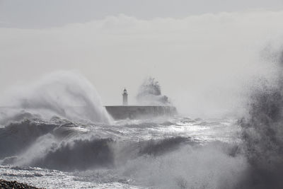 Water splashing in sea against cloudy sky