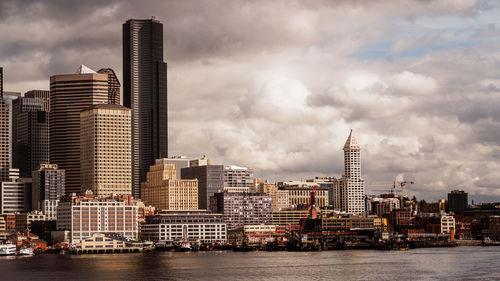 Modern buildings by river against sky in city