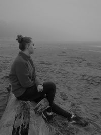 Woman sitting on rock looking longingly at sea shore against sky