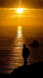 Silhouette man standing on cliff against sea during sunset